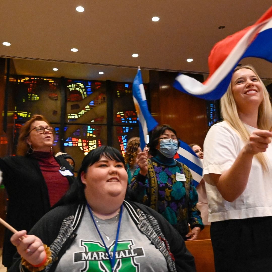 Young women holding flags of other countries at a chapel service.